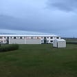 An old barracks outside Reykjavík, Iceland. White building with grass in the foreground and an Icelandic summer night sky in the background. Heavy clouds, bright sun (for midnight), and a gloomy night.