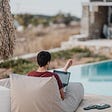 A digital nomad sits behind his laptop overlooking a swimming pool