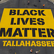 An overhead view of an intersection in Tallahassee. A yellow square is filled with black text stating “Black Lives Matter” Tallahassee.