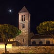 Detailed illustration of a church, with a tower and two trees, under the moonlight at night.