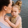 A Mum kissing her three year old daughter on the forehead.