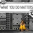 Photo shows a woman sitting below wall art that says “What you do matters.”