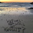 Image of a beach with the words: What do you want? written in the sand