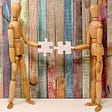 Two wooden dolls holding intersecting puzzle pieces.
