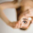 Woman’s eye in focus, body is out of focus. Her eye is framed by her hands being held out in front of her. The body is upside down but the eye is right side up.