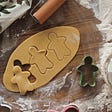 Gingerbread men being cut out of dough with cookie cutters