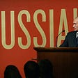 Putin speaking in front of a Russia! banner