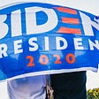 Two people hidden behind “Biden President 2020” banner