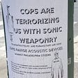 A poster reading, “Cops are terrorizing us with sonic weaponry.”