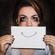 crying woman with sign showing a happy face in front of her mouth