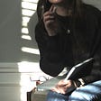 Woman sitting with a notebook journal on lap and pen in hand, in the light and shadow from window blinds