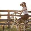 A young girl with virtual reality glasses on riding a bike next to an open field.