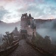 A cobbled pathway leads to a castle rising above the mist