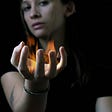 Woman in a black t shirt with arm out stretched and hands up, fire in the palm of her hand.