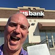 Me in center with big smile standing in front of a US Bank and holding the deposit slip of my first business check received.