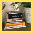 A pile of books on a table next to a plant