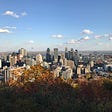 The skyscrapers of Montreal as seen from Mount Royal, in the fall, under a blue sky with a few white clouds.