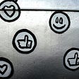 Social media icons including a smiley face, hearts, and thumbs up are painted in black and white on a metal surface.