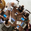 Teamwork image of a group of people in a meeting working together on a wooden table with computers, tablets and smartphones