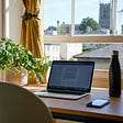 A virtual office remote worker’s work from home set up by an open window with a laptop, a plant and a water bottle.