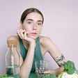 Thin girl sitting behind a cup of water and raw vegetables.