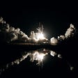 Nighttime Space Shuttle launch with fuel clouds and reflection