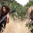 Two women from the all-female heavy metal band, Slave to Sirens, playing guitar in a field.