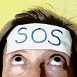 SOS written on masking tape stuck on forehead with eyes looking up towards it