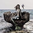A Siren sitting on a rock talking with a Pixie