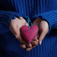 Woman wearing a blue sweater, holding a quilted heart with the word “Love” stitched into it