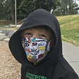 A smiling child in a hoodie and cloth mask printed with comic book character’s speech bubble reading, “It’s now or never.”