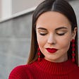 Woman with perfect makeup and bright red, matching lipstick, earrings, and sweater.