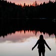 woman with arms out facing lake