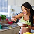 Woman eating bowl of food in kitchen