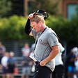 Jon Gruden taking off his visor appearing frustrated on the football field.