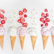 Six alternating strawberry and vanilla ice cream cones with pieces of strawberries and vanilla flowers above them.