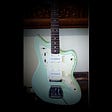 Seafoam green electric Nash guitar leaning against white wall.