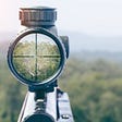A look through a rifle scope with cross hairs honing in on a distant target.