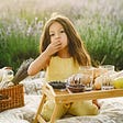 A child in a field eating and enjoying a tray of fruits.