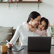 A woman working from home while hugging her daughter.