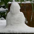 Small snowman on a snow-covered garden table.