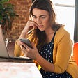 A stressed White woman biting her nails while looking at her cell phone.