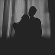 A black and white of two people’s silhouettes in front of a curtained window.