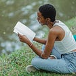 Person reading a book by a lake.