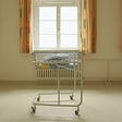 An empty baby bed in front of a window in a maternity ward.