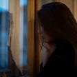 A photo of a sad woman with long hair looking out the window.