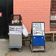 A small cart with signs in English and Spanish that say “free food”/”comida gratis.”