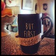 Black coffee mug depicting ‘But First Coffee’ with ‘tea’ written on a piece of tape over the word coffee.