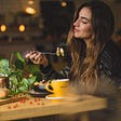 Young woman with long hair enjoying coffee and food in a restaurant with modern decor.