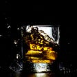 A glass of bourbon on the rocks, on a black background.